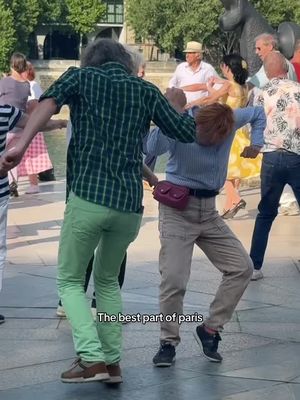 The cover image shows a group of people dancing in a public space, likely a plaza or street in Paris. Two central figures are focused on, a person in green pants and a plaid shirt and another with tan pants, a light blue shirt wearing a fanny pack across the body. They are mid-dance with the other people around them, there are also other people in the background.