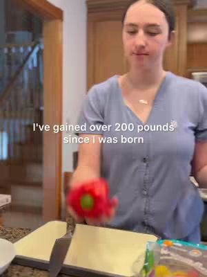 A woman in a blue top is standing in a kitchen setting. She holds a red bell pepper, with text overlayed. The background includes kitchen cabinets and a door.