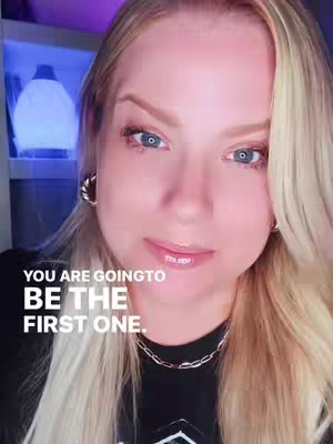 A close-up shot of a woman's face, slightly angled. She has blonde hair, light skin, and blue eyes. She's wearing small gold hoop earrings and a silver chain necklace. The background includes a softly lit white object and a hint of a cabinet or shelf. Text overlays in the bottom middle, in a bold white font. Her expression is calm and inviting.
