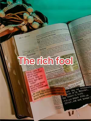 An open book with highlighted and annotated pages, along with colorful sticky notes. The phrase 'The rich fool' is overlayed across the pages in a bold, red font.
