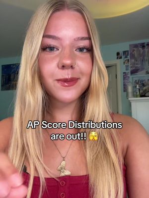 A young woman with long blonde hair is centered in the frame. Text overlayed reads "AP Score Distributions are out!!" She is wearing a red top, and a gold butterfly pendant is visible.