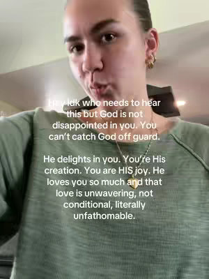 The video shows a selfie-style shot of a person wearing a green top with text overlayed. The person is looking towards the camera, and the text appears in a white font. The background is blurred, but gives a sense of a neutral interior space.