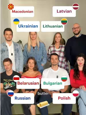 A group of people stand in front of a blurred background. Each person is positioned below a text label indicating a language. There is a stick of butter placed in front of the group.