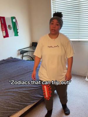 A woman stands in a room with a bed and window. A Mexican flag hangs on the wall. The woman is wearing a tee shirt and sweat pants.