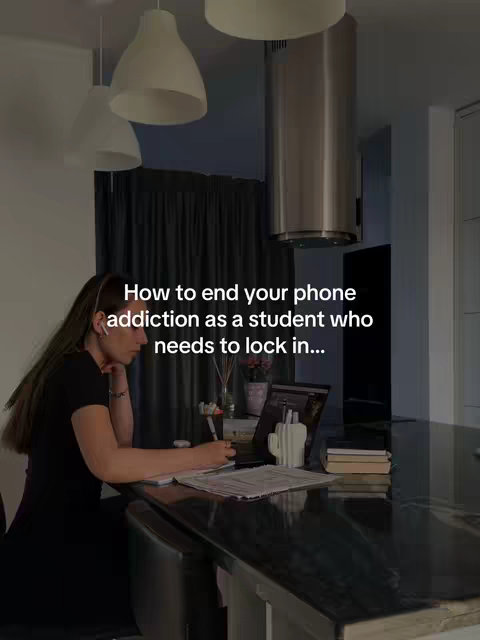 A well-lit interior shot features a woman sitting at a kitchen counter, working on a laptop and writing on a notepad. The counter is black, lined with a few items, facing a dark-colored curtain. Above, white lamps hang from the ceiling. The main text states, 'How to end your phone addiction as a student who needs to lock in...'