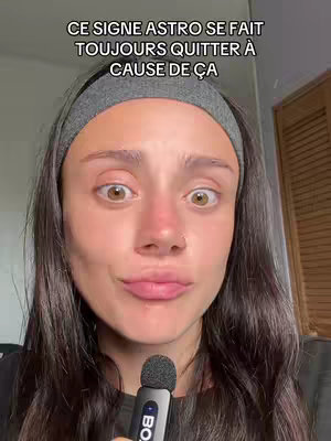 A woman with dark hair and a gray headband is centered, looking directly at the camera with wide eyes and a slightly surprised expression. She is holding a microphone. Text overlays the image, and the background appears to be a room.