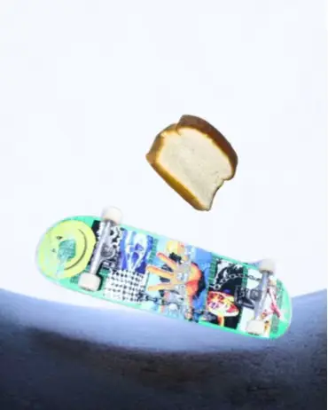 A photo shows a green skateboard in the lower part of the image, slightly angled towards the top right. A piece of bread is floating above it. The background is a gradient of light blue to white.