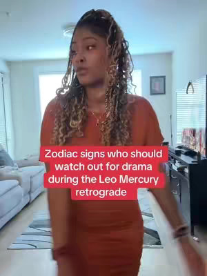 A person stands in a living room, facing slightly towards the camera. They wear an orange dress. The background has a couch, window, and a TV. A red text overlay near the bottom of the image.
