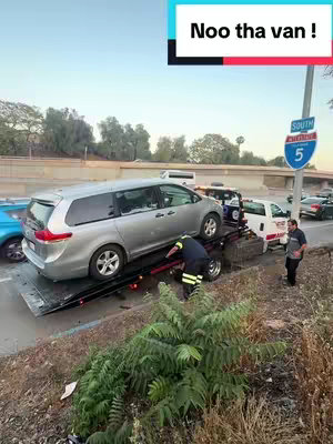 A silver minivan is being loaded onto a tow truck on the side of a highway. A firefighter in high-visibility gear gestures near the car. A sign for "South I-5" is visible, indicating the highway. Other cars and personnel are present in the scene.