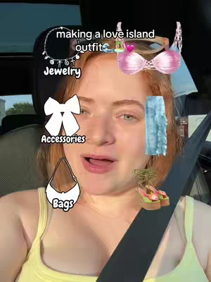 A selfie-style shot of a young woman inside a car; she has fair skin, red hair, and is wearing a yellow top and a seatbelt. Text and graphics of clothing items are overlaid, including a necklace, swimsuit top, bow, pants, purse, and sandals. The background is the interior of the car.