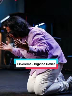 The image shows a person kneeling on a dark surface with their hands raised, appearing to be in a devotional or worship posture. The person is wearing a long sleeve shirt and light colored pants. The background is blurry, suggesting a low depth of field. A text overlay at the bottom identifies the content as a "Ekwueme - Bigvibe Cover."