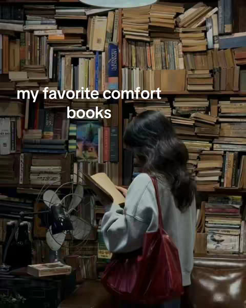 A person is standing in a room filled with bookshelves. The person is facing away from the camera, reading a book. Above them is the text overlay 'my favorite comfort books'.