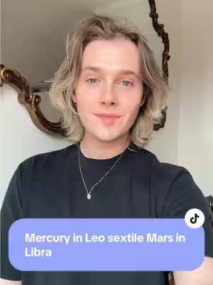 A medium shot of a person with blonde hair, wearing a black shirt and a silver necklace. The person has a neutral expression and is looking directly at the camera. A blue rectangle with white text at the bottom of the frame reads 'Mercury in Leo sextile Mars in Libra.' In the background, a gold-colored mirror is visible, and on the top right is the TikTok logo.
