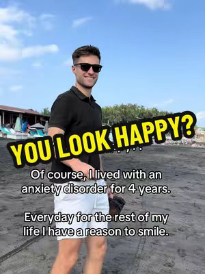 A man in sunglasses and a black shirt stands on a dark beach, smiling. Text overlays in an eye-catching yellow font. The background features a sky partly covered by clouds and some structures.
