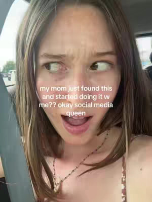 A close-up shot of a young woman's face from a low angle. She gazes off to the side with a surprised expression, her mouth slightly open. Text overlays are present near the top of the frame. Her hair is centered, and framed by the car's interior visible in the background.