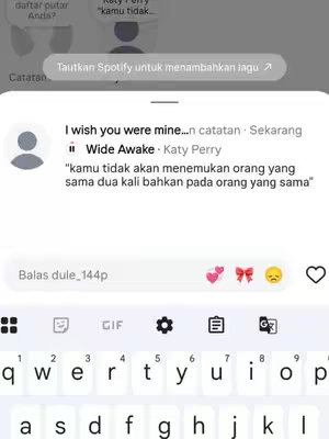The image shows a phone screen. At the top is a notification in a gray rectangular box, featuring the text 'Tautkan Spotify untuk menambahkan lagu' (Translate to 'Link Spotify to add songs').  Below this is a chat message, with the text 'I wish you were mine... Katy Perry Wide Awake' and a quote. At the very bottom is a keyboard and text input area with some emojis like hearts.