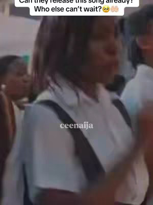 The cover image presents a slightly blurred, medium shot capturing a group of people, their focus directed towards something out of frame. The central figure is a person with short, dark hair wearing a white top and black straps. They are in the foreground, and they appear to be in a public space. The overall lighting seems natural, and the composition is typical of a candid moment. There is overlaid text positioned at a diagonal angle to the top, which has a question and an emoji.