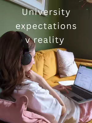 A young woman with brown hair wearing headphones sits on a yellow couch, looking at a laptop. The text overlay reads: "University expectations v reality". The setting appears to be a well-lit room with a green wall.