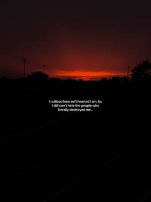 A dark, moody image featuring a nighttime sky with a vibrant red and orange sunset. Silhouetted against the sky are light poles and trees. In the foreground, a dark, possibly grassy area leads to the bottom of the frame where text is overlaid in white, small font.