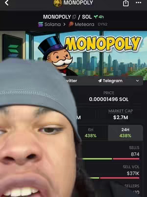 A selfie-style shot with a man wearing a gray beanie, looking at the camera with an open mouth. Behind him is a digital display showing information about a cryptocurrency called Monopoly, with a logo featuring a Monopoly character. The background shows a cityscape graphic.