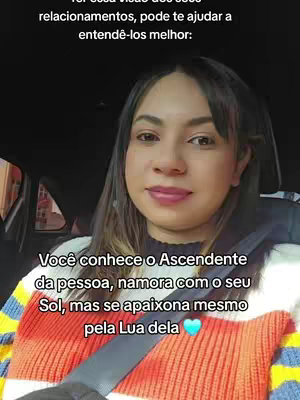 A woman sits in a car, facing the camera. The image is a selfie-style shot. The woman is wearing a tri-colored sweater—orange, white, and blue. Text overlays are added at the top and bottom, and in the top, a second message is given, which seems to be part of the video content. Inside the car, the darkness is dominant to create a simple contrast with the figure and the text. The overall composition is clear and focused on the subject.
