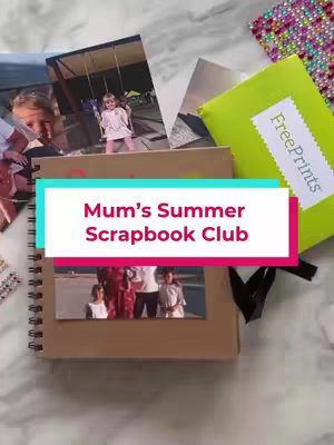 The image is a top-down shot of a table. The focus is on a partially open scrapbook with photos and decorative elements. A light green envelope with "FreePrints" printed on it, along with loose photos, is visible, with a pair of scissors.