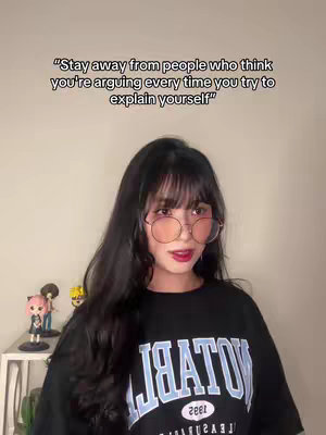 The cover image features a young woman with black hair and bangs, wearing glasses and a black t-shirt with white text. Text overlayed on the image reads a quote. She is positioned in front of a plain white wall with a small shelf holding figurines on the left. The background is neutral, putting the focus on the woman and the text. The overall composition is simple and straightforward with a clear text overlay.