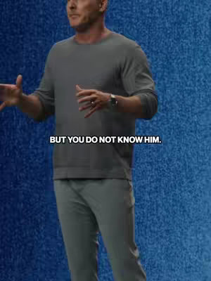 A man in a gray sweater and pants is giving a presentation in front of a blue textured background. Text overlayed at the bottom of the frame says 'BUT YOU DO NOT KNOW HIM.'