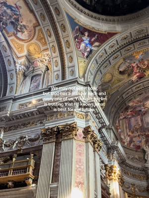 An interior shot of a cathedral with high, ornate ceilings and walls adorned with paintings. The lighting suggests a soft, heavenly glow. In the center of the frame displays a white box with text.