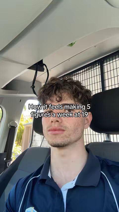 A young man is seated in a vehicle, likely a car. The camera angle is a medium shot, focusing on the person's upper body and face, with the head being the main focus. The interior of the car is visible, with elements of the dashboard and roof overhead. The image has a natural lighting.