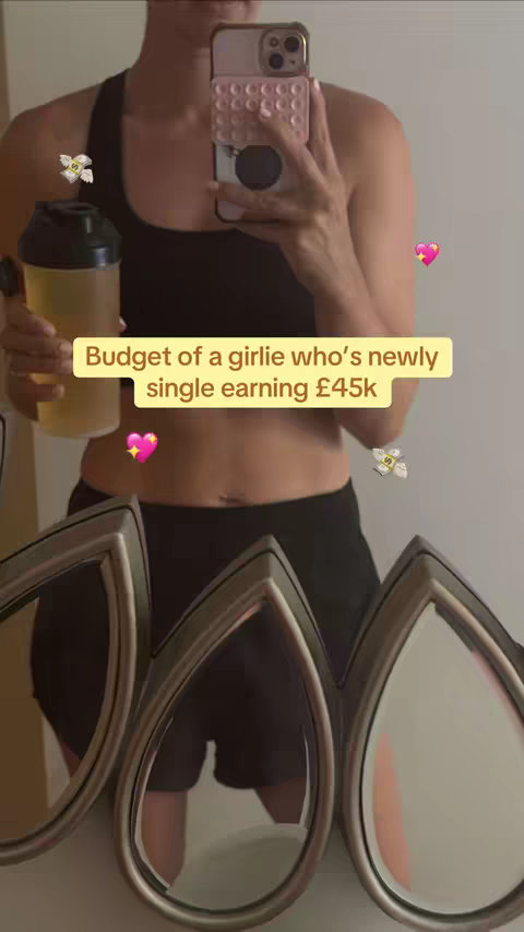 A woman is reflected in a mirror, holding a protein shaker and her phone. The text overlay reads, "Budget of a girlie who's newly single earning £45k."