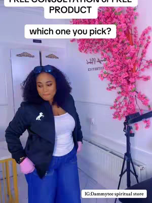 A woman stands in a room with a large pink floral arrangement. She wears a black jacket, white top, and blue jeans. Text overlays are present to create a hook.