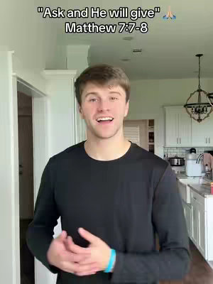 A young man with light brown hair is smiling and speaking in a well-lit interior space. Text overlays the image, quoting a Bible verse. He wears a black shirt and has a blue bracelet on his left wrist.