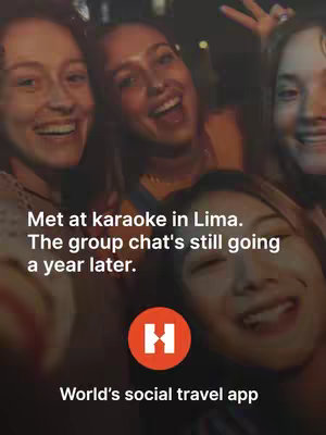 A selfie-style shot featuring five young women close together. They're smiling and appear to be at a party or gathering, with a dark background that suggests it's nighttime or indoors. Text overlays on the image promote the Hostelworld app.