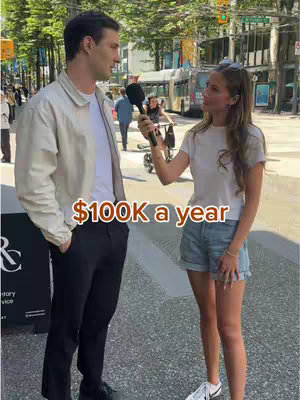 A street scene shows a woman in a white top and denim shorts interviewing a man who has a beige jacket and black pants with a microphone. The added text overlay states '$100K a year'. The background shows a busy street with other individuals, a bus, and buildings.