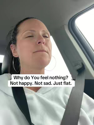 A woman is shown from the chest up, seated in a car. She has dark hair pulled back and is wearing large hoop earrings and a white hoodie. She has a neutral, closed-eyed expression, suggesting contemplation or introspection. A text overlay appears in the bottom left corner stating, "Why do You feel nothing? Not happy. Not sad. Just flat." suggesting the video's topic is emotional numbness.