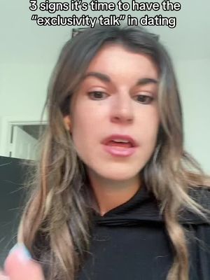 The cover image features a medium close-up of a woman with long, wavy brown hair and a black hoodie. The text overlay states: "3 signs it’s time to have the "exclusivity talk" in dating". The woman appears to be looking directly at the camera with an open mouth and neutral expression. The background is blurred, suggesting an interior setting.