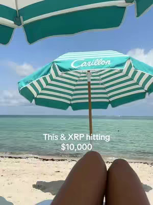 A sunny beach scene with a turquoise umbrella set up, with turquoise and white striped pattern, in front of the ocean. The feet of a person laying down are in the foreground.