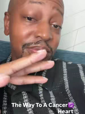 A man with a shaved head and a goatee is close to the camera. Text overlay reads "The Way To A Cancer Heart". The man is wearing a black shirt with a geometric pattern and is seated somewhere with a blue surface.