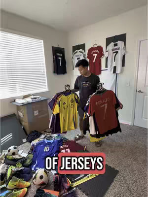 A room with several soccer jerseys prominently displayed, with the creator holding a few more jerseys in the center, a lot of sports clothes on the floor.