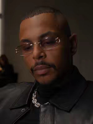 The cover image features a close-up shot of a man with a mustache and glasses, wearing a black turtleneck and a silver chain. He is positioned in the center of the frame against a dark background. The lighting is soft, highlighting his face and jewelry.