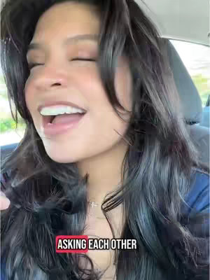 The cover image shows a woman with long, dark hair seated inside of a car, with her eyes closed and mouth open as if singing or speaking enthusiastically. A text overlay at the bottom reads "ASKING EACH OTHER" in white letters contained inside a red rectangle.