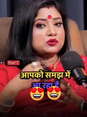 A woman with dark hair and a bindi is holding a microphone, looking directly at the camera. Text overlays in Hindi and playful emojis add context. The background is blurred.