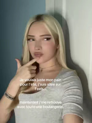 A selfie-style shot of a young woman with blonde hair, gazing off to the side with a thoughtful expression while touching her finger to her lips. Text overlays are present with the Feels app logo in the bottom left.