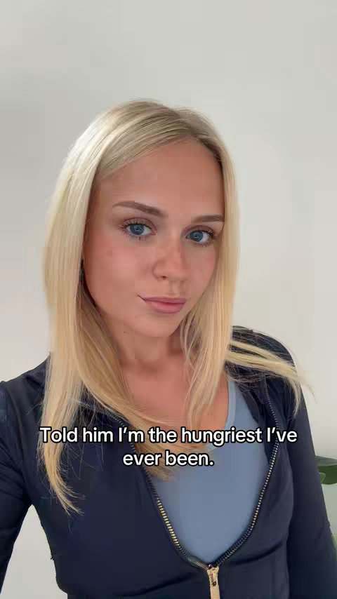 A woman with long blonde hair and blue eyes is  in the front of the camera, wearing a blue top and a dark blue zip-up jacket.  Black text overlayed on the image reads, "Told him I'm the hungriest I've ever been."