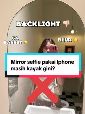 A woman taking a mirror selfie with an iPhone. The image is framed within a round mirror. The woman is holding the phone in front of her face. Above the woman is the text 'Backlight' with a thumbs-down emoji. To the left is the text 'Ga banget' with a thinking emoji. To the right is the text 'Blur' with a worried emoji. At the bottom of the image is a rectangular banner with the words 'Mirror selfie pakai iPhone masih kayak gini?' and an 'X' symbol overlaying the woman's lower body. The color tones are a mix of warm and neutral, reflecting the interior setting.