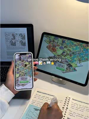 The image shows a workspace with a person's hands interacting with several digital devices. A laptop displaying a document is in the background. In the foreground, a smartphone displays an app view of a map and a FocusTree app. A tablet is at the right, also showing an app view and a timer. A notebook and pen are in active use on the table as well.