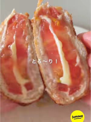 The image showcases a cross-section of a deep-fried dish, likely a meat-wrapped tomato and cheese creation. The core features a vibrant red tomato, layered with a strip of white cheese. The outer layer is golden-brown and crispy, indicating it has been fried. A text overlay "とろ~り!"(Toro-ri!, or Melted!) is placed on the image. The overall composition emphasizes the delicious and visually appealing, highlighting the melty cheese and crispy exterior.