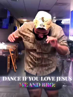 A man in a tan shirt and a cap is dancing in front of a blurred background. Text overlays say, "DANCE IF YOU LOVE JESUS" and "ME AND BRO:" The lighting is dim.