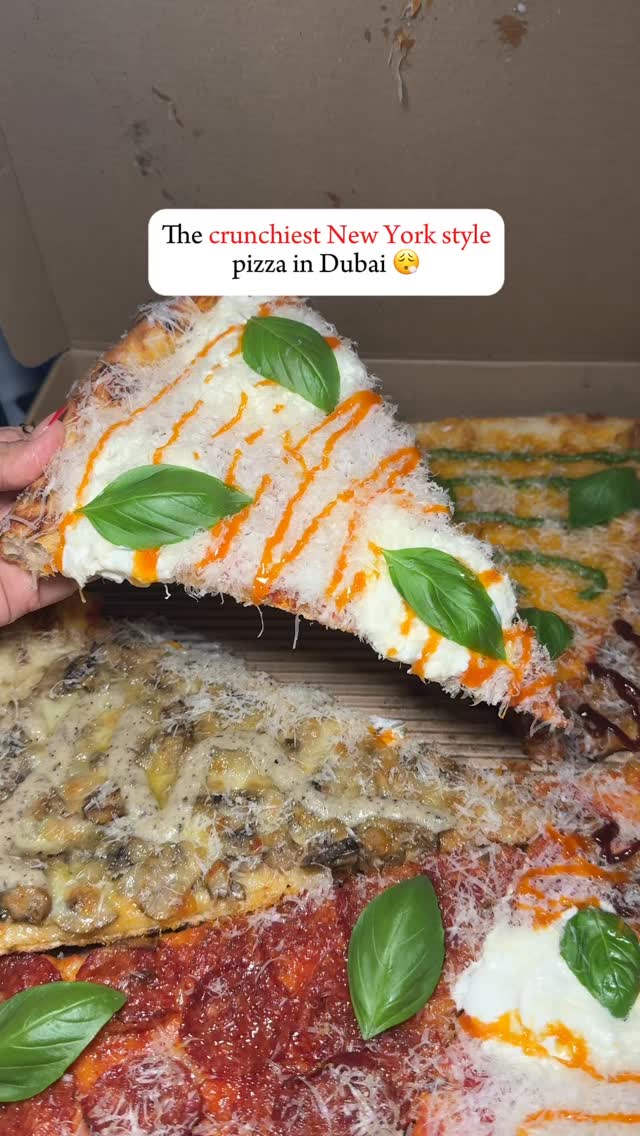 The cover image shows a slice of pizza being held up, showcasing melted cheese with orange sauce drizzled on top, fresh basil leaves, and a crispy exterior. Below the slice, several other pizza slices are visible, displaying different toppings and crusts, all within a pizza box. The overall composition emphasizes the visual appeal of the pizza and its diverse toppings.